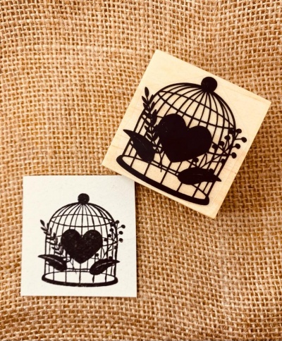 Carimbo de madeira com gaiola, coração e folhagem sobre fundo de juta