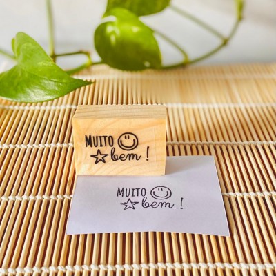 Carimbo de madeira com texto e desenho, e papel com impressão num tapete de vime.