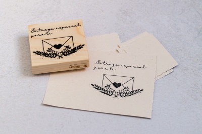 Carimbo de madeira com desenho de envelope e texto 'Entrega especial para ti' e papéis com carimbo
