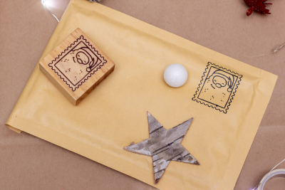 Envelope almofadado amarelo com carimbo em forma de selo postal, estrela decorativa de madeira e bola branca