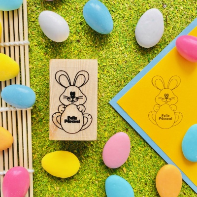 Carimbo de madeira com desenho de coelho e ovos coloridos em fundo verde.