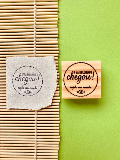 Selo de madeira com carimbo em português e papel com impressão similar sobre esteira de bambu