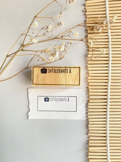 Dois carimbos com texto Intolerante à junto a flores secas e tapete de madeira