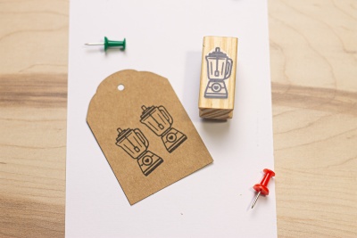 Carimbo de madeira com imagem de liquidificador e etiqueta de papel castanha.