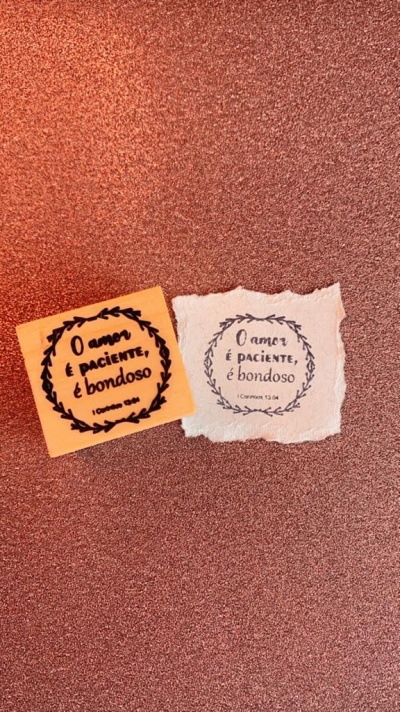 Duas etiquetas em papel com texto 'O amor é paciente, é bondoso' em moldura de folhas sobre fundo cobre texturizado.