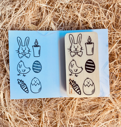 Carimbo de madeira com desenhos de Páscoa sobre cartão azul e palha