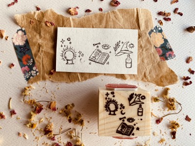 Carimbo de madeira com desenhos de globo, lua, livro, estrelas e plantas em papel kraft com flores secas