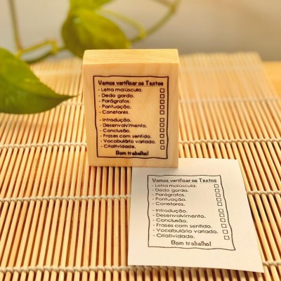 Carimbo de madeira com texto sobre verificação de textos em português colocado sobre esteira de madeira com impressão do texto em papel ao lado