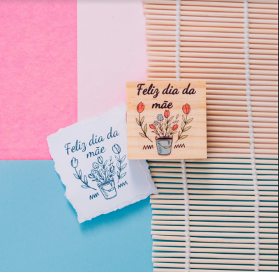 Selo de madeira com ilustração colorida e papel com impressão azul com texto Feliz dia da mãe
