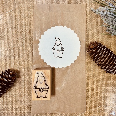 Selo de papel com desenho de duende e carimbo de madeira sobre tecido de ráfia com pinhas