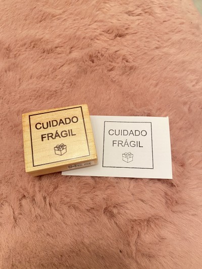 Carimbo de madeira com texto CUIDADO FRÁGIL e ícone de caixa ao lado de impressão do carimbo