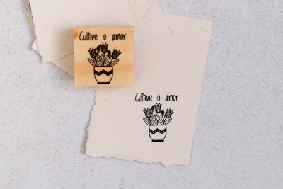 Carimbo de madeira com desenho de flores e texto 'Cultive o amor' ao lado de impressão num papel bege.