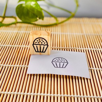 Carimbo de madeira com desenho de muffin e marca carimbada em papel sobre esteira de bambu