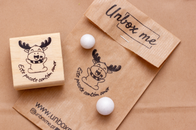 Selo de madeira com desenho de alce e saco de papel com texto Unbox me.