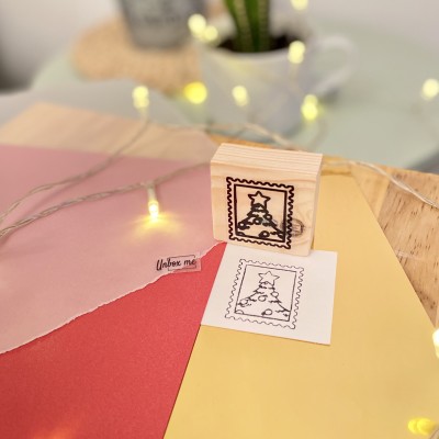 Carimbo de madeira com desenho de árvore de Natal em selo quadrado perto de papeis coloridos e luzes decorativas