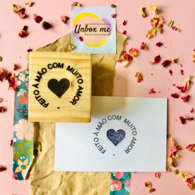 Selo de madeira com texto e coração ao lado de impressão em papel sobre superfície rosa com pétalas secas