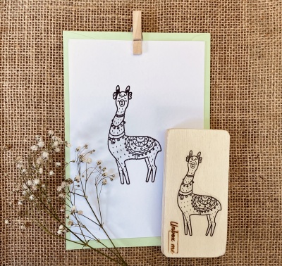 Carimbo de madeira com desenho de lhama e folha com o mesmo desenho sobre tecido rústico