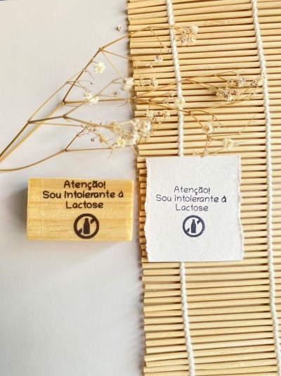 Selo de madeira e impressão em papel com texto sobre intolerância à lactose sobre tapete de bambu e flores secas
