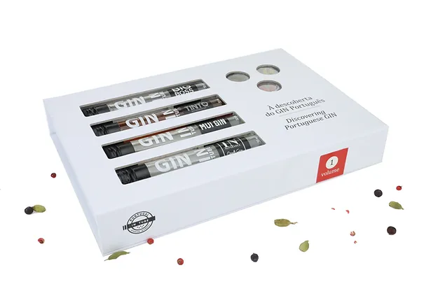 À Descoberta do Gin Português - Volume 1 Caixa branca com quatro tubos de ensaio contendo gin, com texto e especiarias ao redor