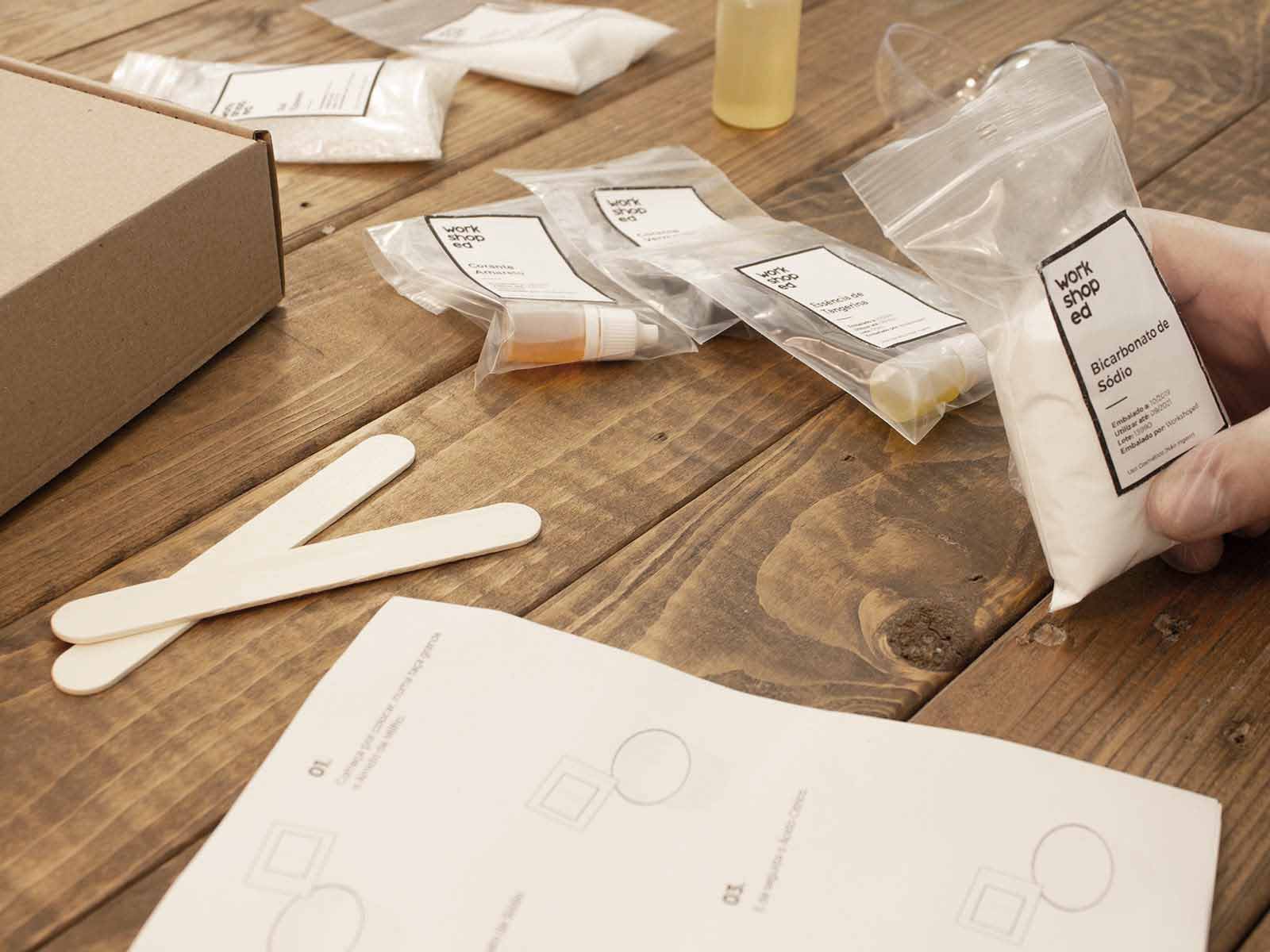 Workshop Box: Velas Aromáticas Kit com sacos plásticos etiquetados, espátulas de madeira, manual e caixa sobre mesa de madeira