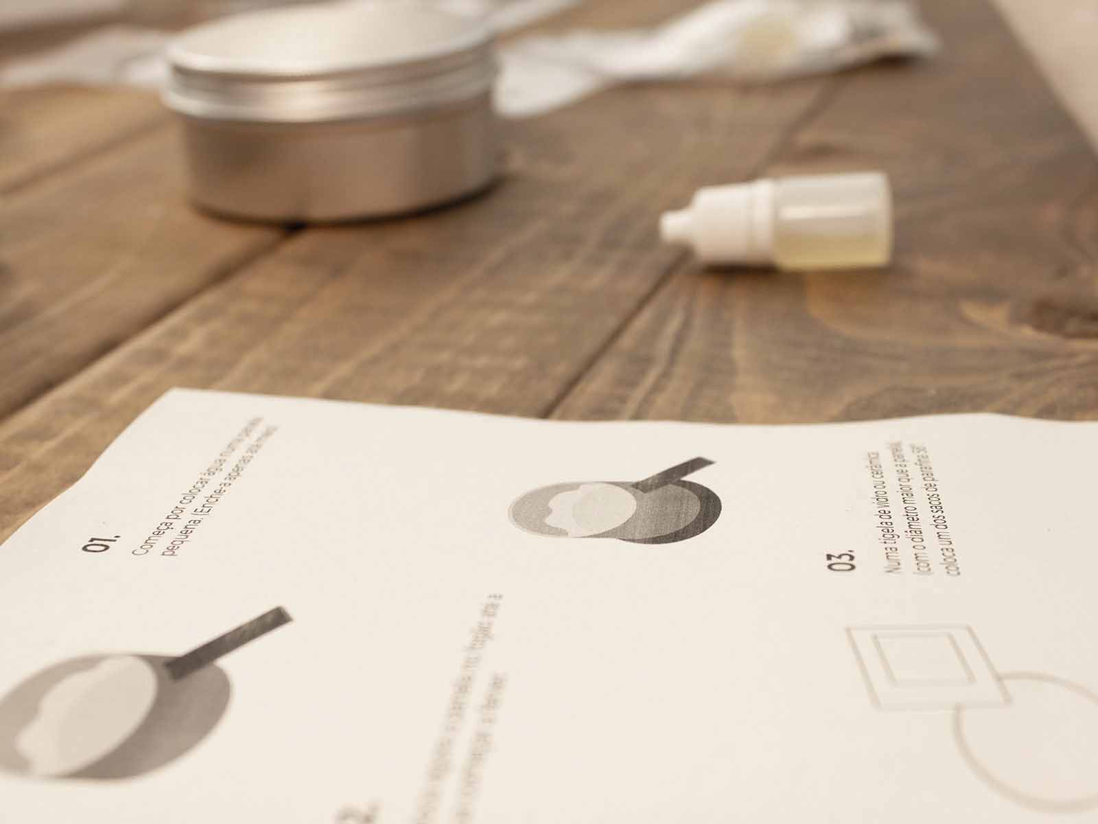 Workshop Box: Velas Aromáticas Folha branca com texto e ilustrações sobre mesa de madeira com frasco e lata ao fundo