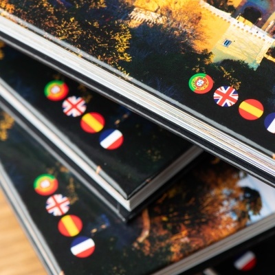 Livros empilhados com capas escuras mostrando bandeiras de Portugal, Reino Unido, Espanha e França.