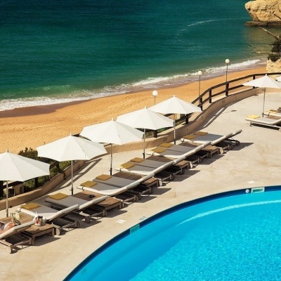 Espreguiçadeiras de praia com guarda-sóis brancos junto a piscina e praia