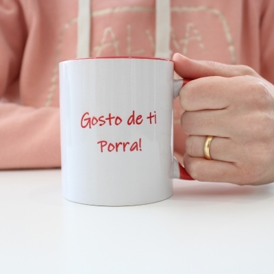 Caneca branca com texto 'Gosto de ti Porra!' segurada por mão com anel dourado