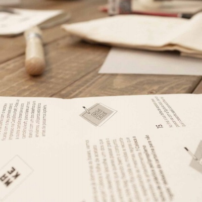 Folhas de papel branco com texto e ícones sobre mesa de madeira, pincel ao fundo