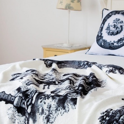 Cobertor branco com padrão preto e almofada decorativa numa cama branca em quarto