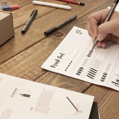 Mesa de madeira com bloco de papel para calligraphy e canetas criando traços e letras