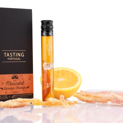Produto Moscatel Laranja em embalagem com caixa e tubo ao lado de uma laranja cortada e cascas cristalizadas.
