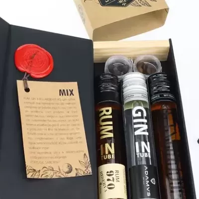 Conjunto de três tubos de vidro com bebidas alcoólicas dentro de caixa preta e madeira claro