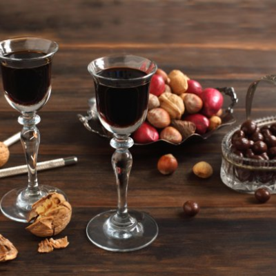 Duas taças de licor escuro, frutos secos e amêndoas cobertas de chocolate sobre mesa de madeira