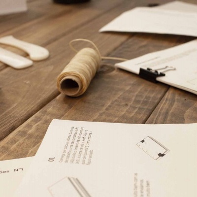 Mesa de madeira com rolo de barbante e papéis com texto e desenhos