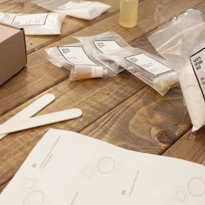 Kit com sacos plásticos etiquetados, espátulas de madeira, manual e caixa sobre mesa de madeira