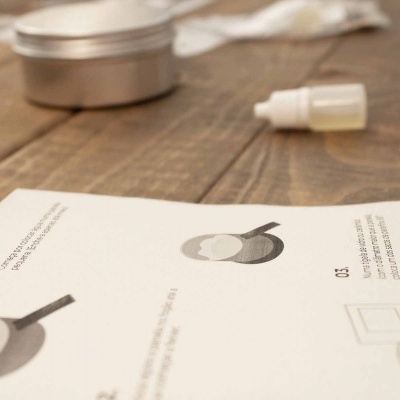 Folha branca com texto e ilustrações sobre mesa de madeira com frasco e lata ao fundo