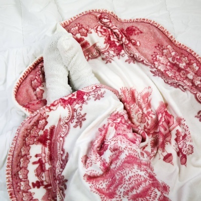 Cobertor branco com padrão floral vermelho e rosa sobre superfície branca acolchoada