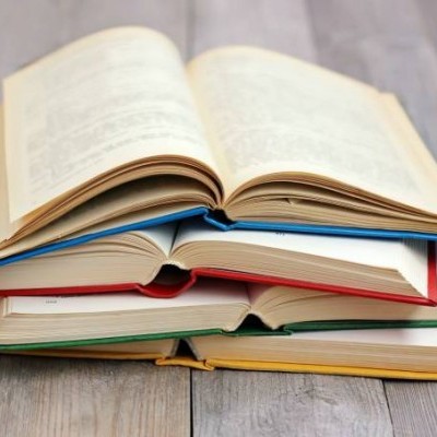 Pilha de livros abertos com capas coloridas sobre chão de madeira