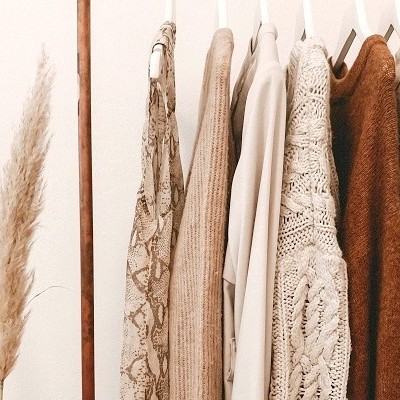 Roupa pendurada em cabide com tons neutros e texturas variadas ao lado de ramos secos