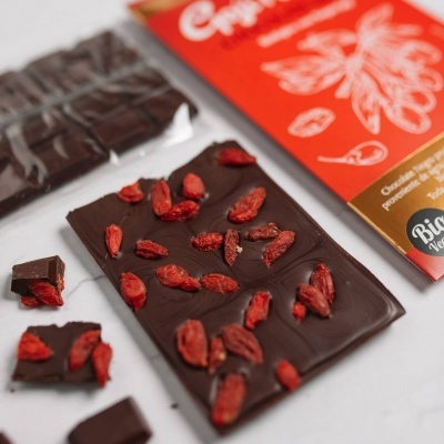 Barra de chocolate preto com bagas vermelhas secas e embalagem colorida ao fundo