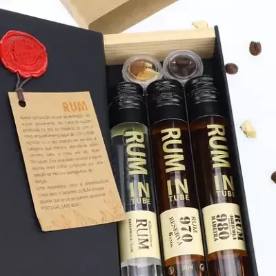Caixa preta com três tubos de ensaio de rum e especiarias sobre fundo branco com grãos de café