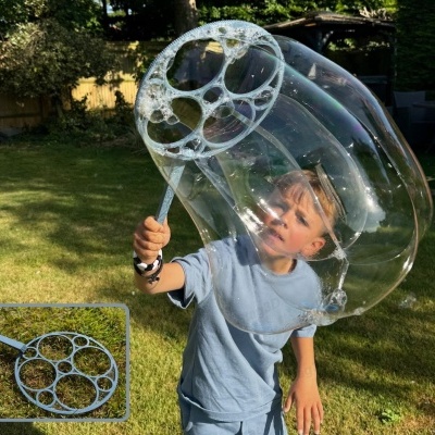 Criança a fazer bolhas de sabão grandes com anel de plástico no jardim