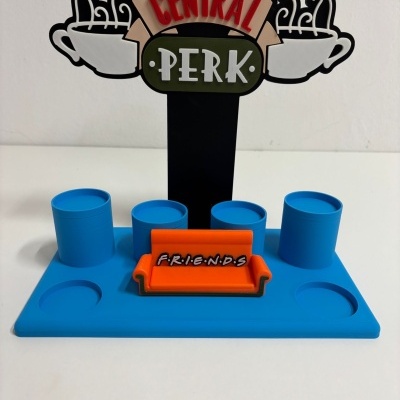 Suporte azul com sofá laranja e placa Central Perk com chávenas de café