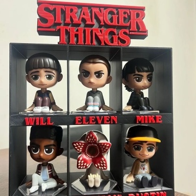 Figuras colecionáveis de Stranger Things em estante preta com nomes e logo da série