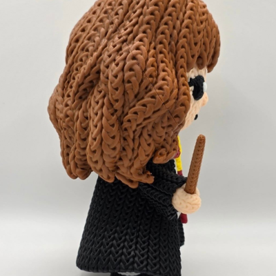 Figura crochetada de personagem com cabelo castanho e vestido preto com varinha