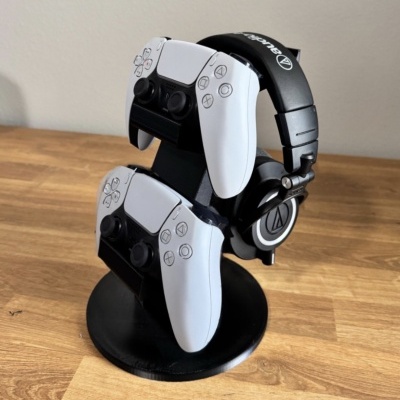 Suporte preto com dois comandos brancos e auricular preto sobre superfície de madeira.