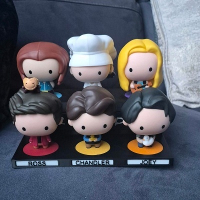 Seis figuras de vinil de personagens com base nomeada ROSS, CHANDLER, JOEY, diferentes cores e pequenos objetos nas mãos.