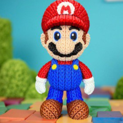 Figura do personagem Mario em tricot com gorro vermelho e roupa azul em cenário colorido