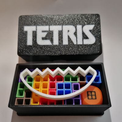 Caixa preta com tampo escrito TETRIS e peças coloridas do jogo Tetris